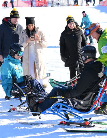 <p>Karwai Tang/WireImage</p> Meghan Markle takes a photo of Prince Harry sit-skiing in Canada on Feb. 14, 2024