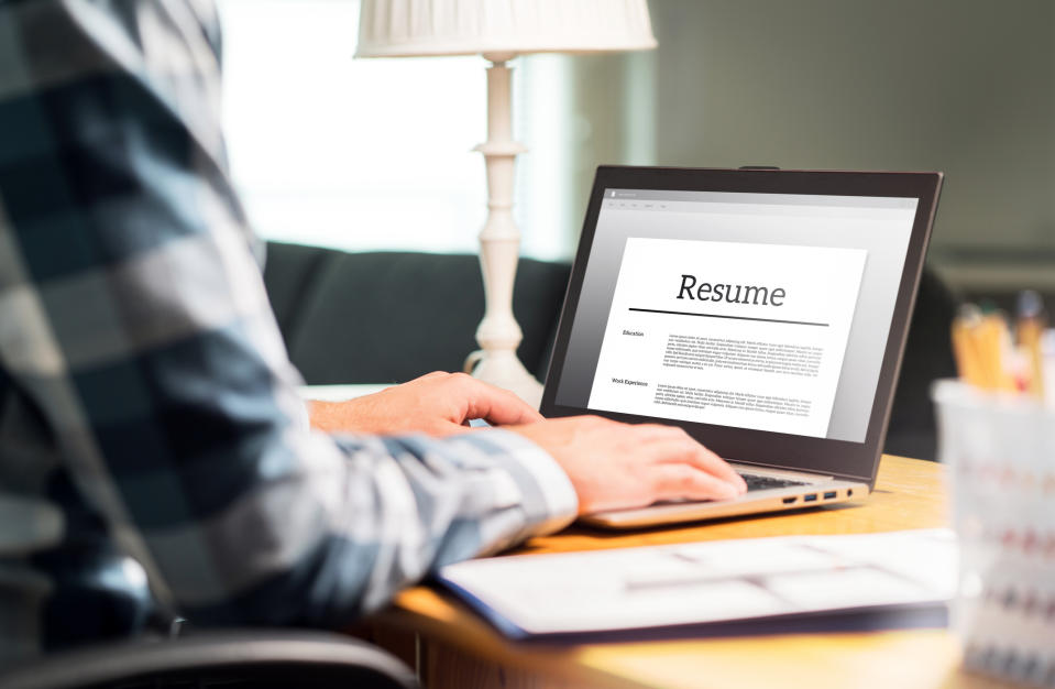 A person is working on a resume on a laptop at a desk. The focus is on the screen displaying the resume application