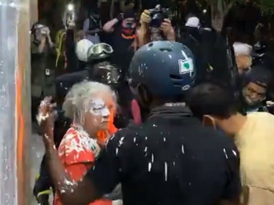 A woman stands in front of a crowd of protesters after they allegedly threw white paint on her: (Portland Police - Twitter)
