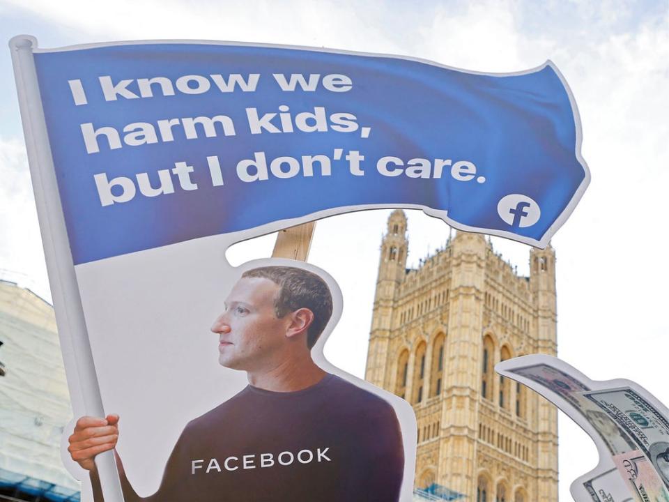 A demonstrator poses with an installation depicting Facebook founder Mark Zuckerberg surfing on a wave of cash and surrounded by distressed teenagers, during a protest opposite the Houses of Parliament in central London on October 25, 2021 (AFP via Getty Images)