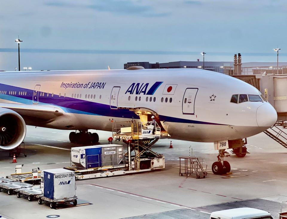 A white ANA Boeing 777-300ER being loaded with baggage at the gate at Tokyo's Haneda airport.