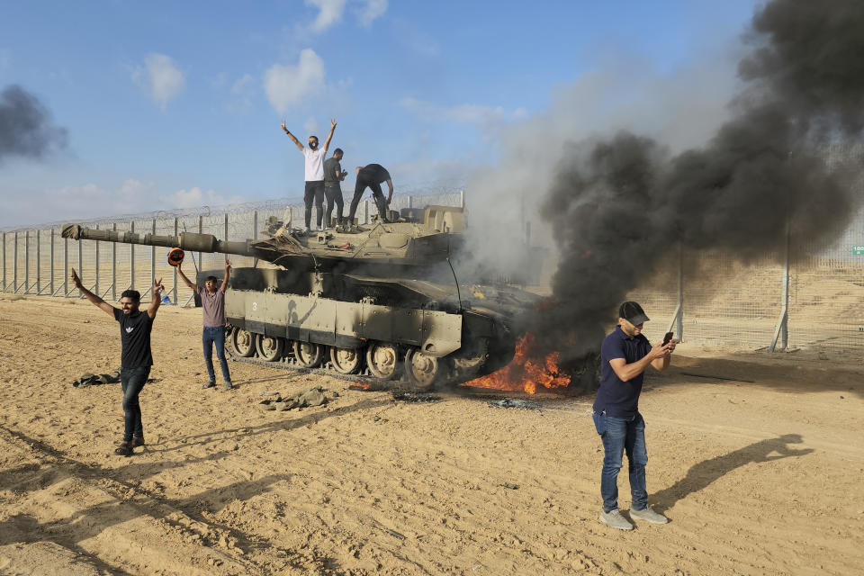 FILE - Palestinians celebrate by a destroyed Israeli tank at the Gaza Strip fence east of Khan Younis Saturday, Oct. 7, 2023. The militant Hamas rulers of the Gaza Strip carried out an unprecedented, multi-front attack on Israel at daybreak Saturday, firing thousands of rockets as dozens of Hamas fighters infiltrated the heavily fortified border in several locations by air, land, and sea and catching the country off-guard on a major holiday. (AP Photo/Hassan Eslaiah, File )