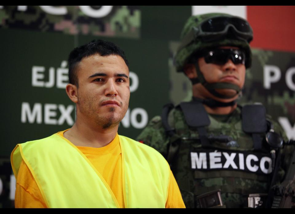 An Army soldier stands next to Daniel Ramirez, alias "El Loco," during his presentation to the media in Mexico City, Monday, May 21, 2012. Ramirez is believed to be a member of the Zetas drug cartel allegedly involved in the dumping of more than 40 hacked-up bodies on a highway outside the city of Cadereyta near Monterrey. The bodies with their heads, hands and feet hacked off were found May 13. (AP Photo/Alexandre Meneghini)