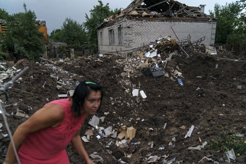 Olga Rudneva walks along the edge of a crater Thursday, Aug. 18, 2022, from a rocket strike yesterday in Druzhkivka, Donetsk region, eastern Ukraine, as Russian shelling continued to hit towns and villages in Donetsk province, regional officials said. (AP Photo/David Goldman)