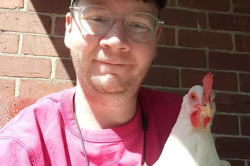 A man holding a chicken smiles at the camera