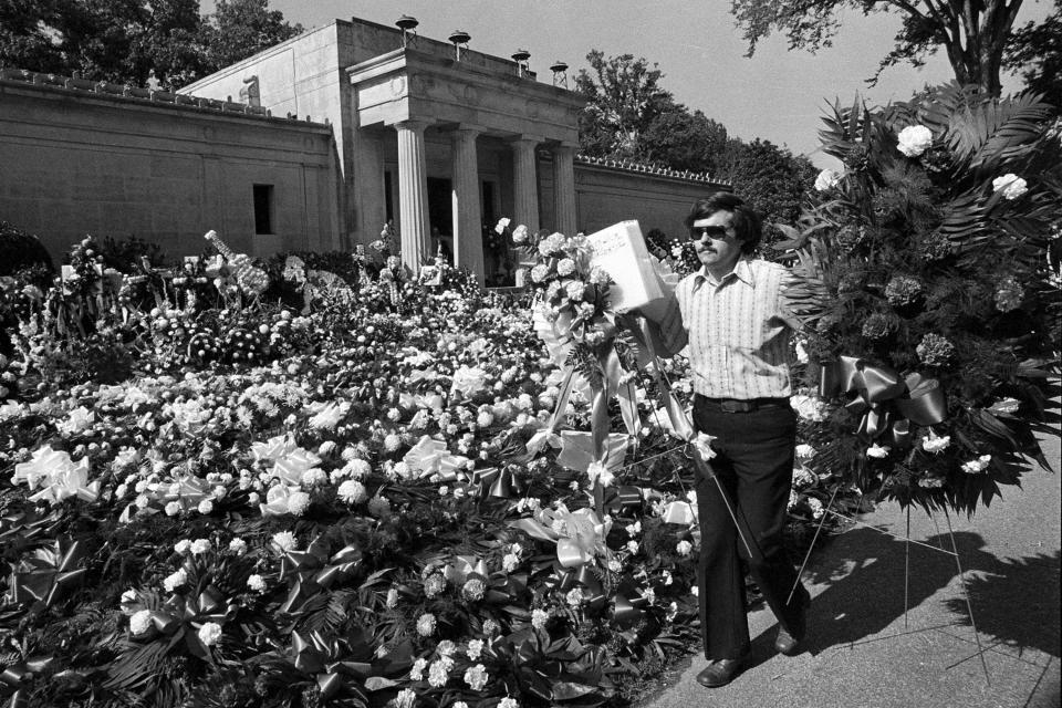 FILE - A florist adds more floral arrangements to the overflowing collection of flowers that cover the ground at the mausoleum Aug. 18, 1977, where singer Elvis Presley will be entombed during funeral services today in Memphis, Tenn. (AP Photo, File)