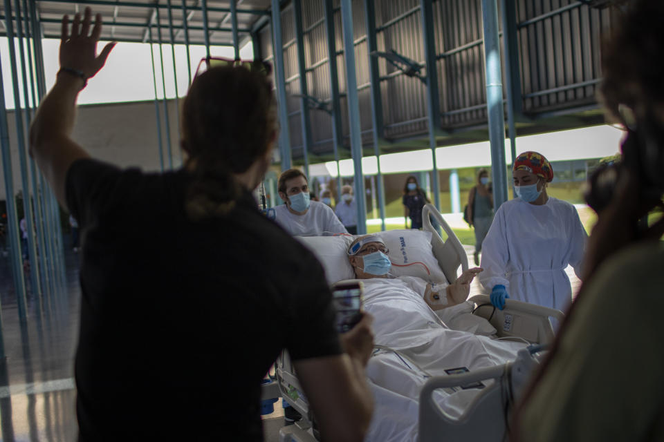 A friend waves at Francisco España, 60, as he is transported to see the Mediterranean sea at the "Hospital del Mar" in Barcelona, Spain, Friday, Sept. 4, 2020. A hospital in Barcelona is studying how short trips to the beach may help COVID-19 patients recover from long and traumatic intensive hospital care. The study is part of a program to “humanize” ICUs. Since re-starting it in early June, the researchers have anecdotally noticed that even ten minutes in front of the blue sea waters can improve a patient’s emotional attitude. (AP Photo/Emilio Morenatti)