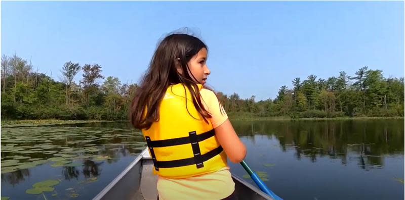 A camper at Lansing School District’s Ebersole Environmental Education Center in Wayland paddles a boat across the lake at the facility, shown in a video screenshot.