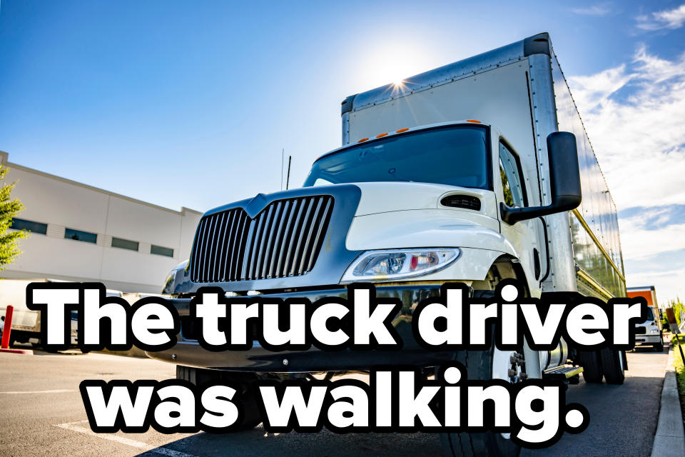 A large commercial truck parked in an industrial area on a sunny day, with a warehouse building visible in the background