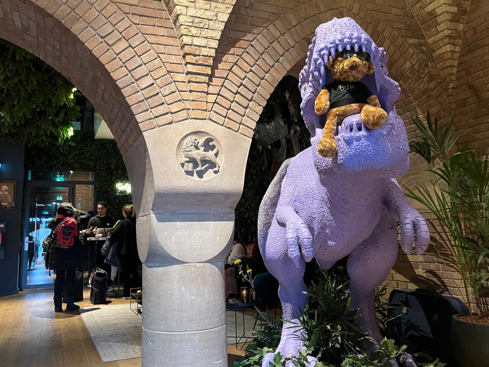 Purple T-rex statue with a teddy bear in its mouth in common area in hotel