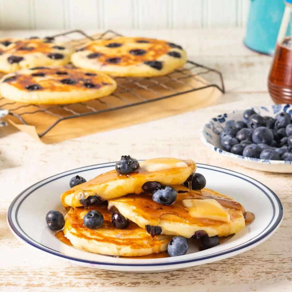 blueberry pancakes on plate with pancakes on wire rack in back