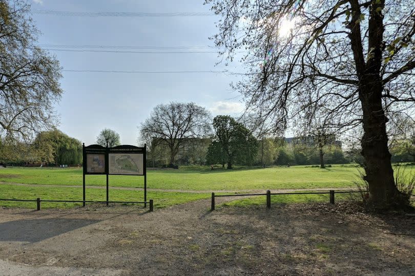 An area of grassy park with an information sign and a tree in the foreground