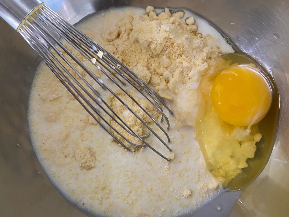 Egg in milk in bowl with Jiffy's cornbread mix being whisked in silver bowl