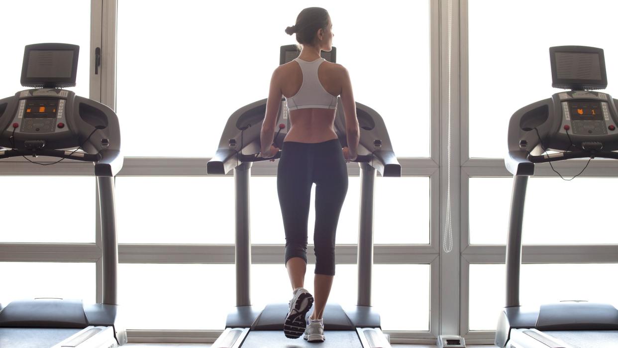  Woman walking on treadmill in a gym in front of window. 