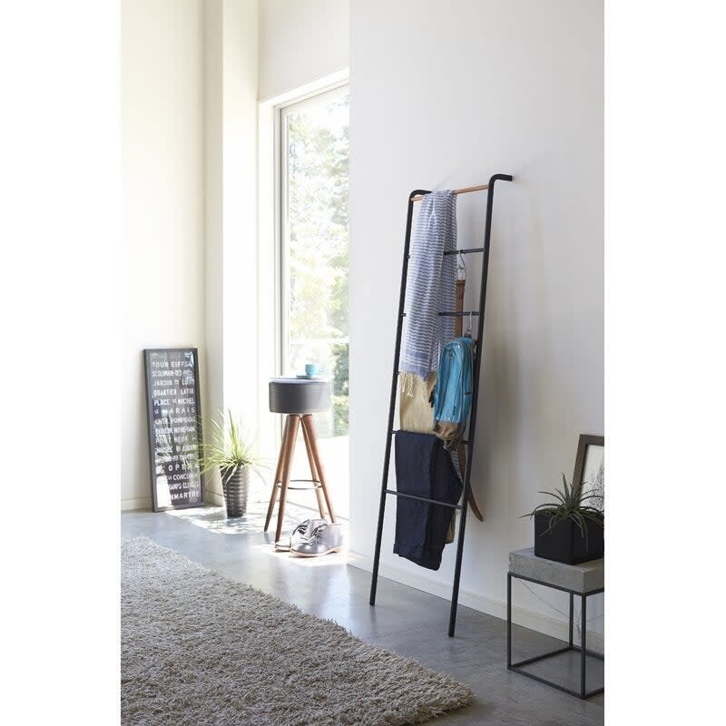 Black blanket ladder propped up against a wall with accessories hung on it