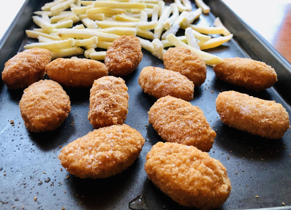 A baking tray with arranged chicken nuggets and French fries, ready to be cooked