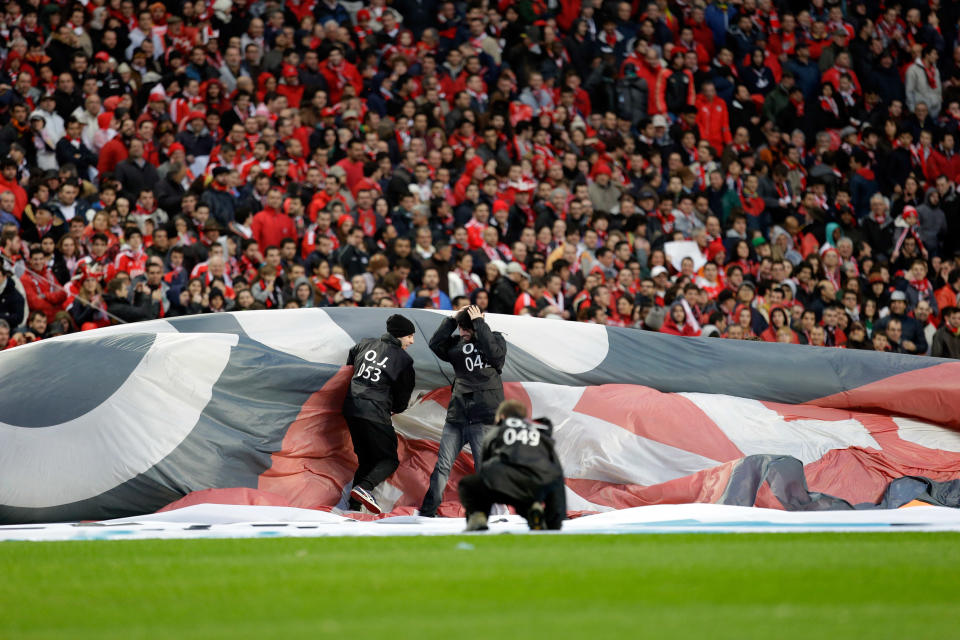 Workers holding an advertising banner struggle with the wind before the start of the Portuguese league soccer match between Benfica and Sporting Sunday, Feb. 9 2014, at Benfica's Luz stadium in Lisbon. Strong winds damaged the stadium roof before kick off and debris fell on the pitch and stands. It was decided the match should be postponed for safety reasons. (AP Photo/Armando Franca)