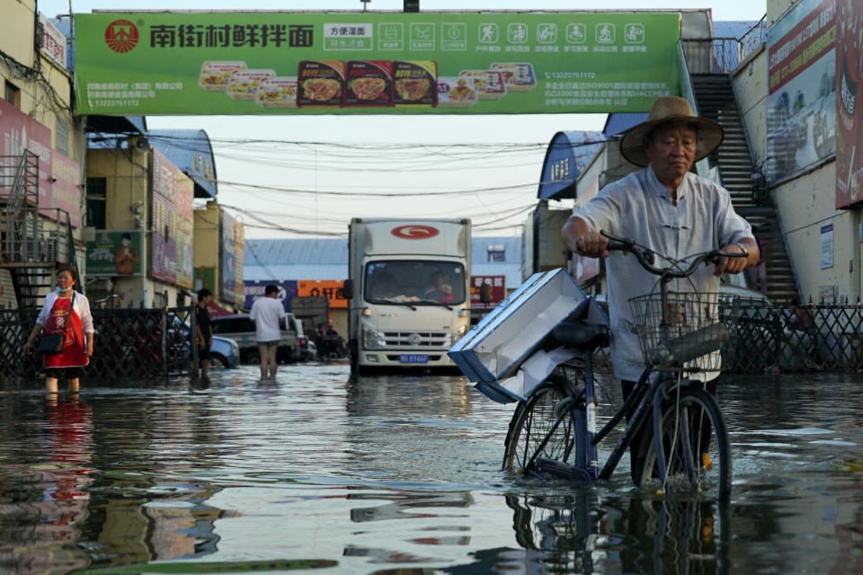 FILE - In this Monday, July 26, 2021 file photo, a man carries goods on his bicycle as he walks out of the the Yubei Agricultural and Aquatic Products World in Xinxiang in central China's Henan Province. Scientists say there’s something different this year from the recent drumbeat of climate weirdness. This summer a lot of the places hit by weather disasters are not used to getting extremes and many of them are wealthier, which is different from the normal climate change victims. That includes unprecedented deadly flooding in Germany and Belgium, 116-degree heat records in Portland, Oregon and similar blistering temperatures in Canada, along with wildfires. Now Southern Europe is seeing scorching temperatures and out-of-control blazes too. And the summer of extremes is only getting started. Peak Atlantic hurricane and wildfire seasons in the United States are knocking at the door. (AP Photo/Dake Kang, File)