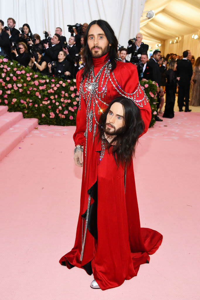 a gown and carrying a mannequin head of himself