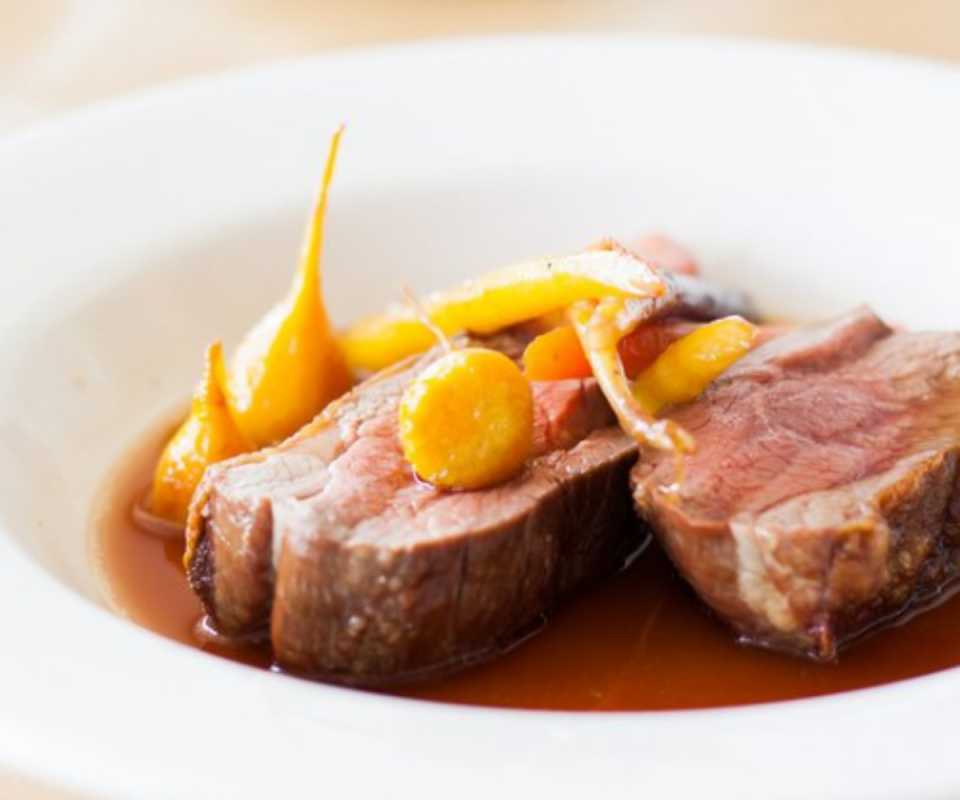 Sliced meat with carrots ontop in a white bowl.