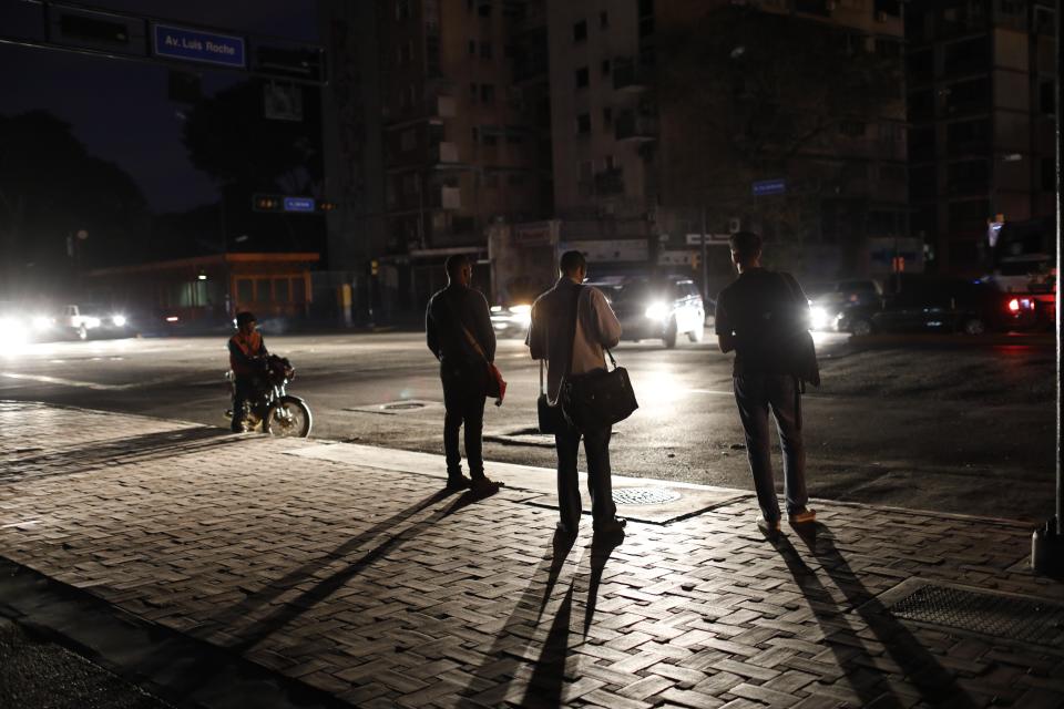 People wait for a public transportation on a street during a blackout in Caracas, Venezuela, Monday, July 22, 2019. The lights went out across much of Venezuela Monday, reviving fears of the blackouts that plunged the country into chaos a few months ago as the government once again accused opponents of sabotaging the nation's hydroelectric power system. (AP Photo/Ariana Cubillos)