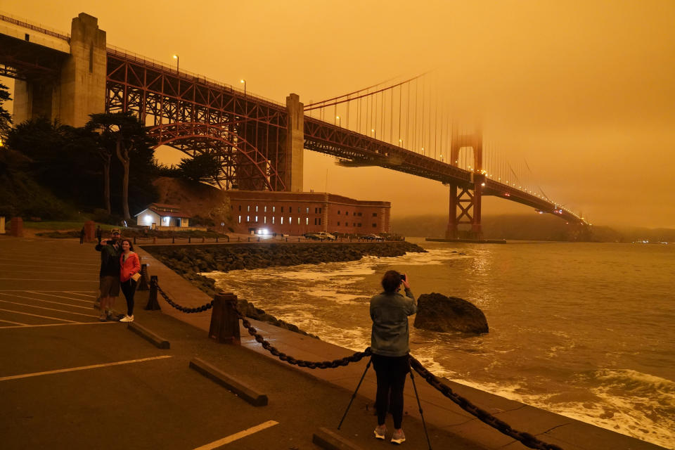 FILE - In this Sept. 9, 2020, file photo, taken at 11:25 a.m. people stop near Fort Point to take pictures of an orange sky over the Golden Gate Bridge caused by heavy smoke from wildfires in San Francisco. Wildfires that scorched huge swaths of the West Coast churned out massive plumes of choking smoke that blanketed millions of people with hazardous pollution that spiked emergency room visits and that experts say could continue generating health problems for years. An Associated Press analysis of air quality data shows 5.2 million people in five states were hit with hazardous levels of pollution for at least a day. (AP Photo/Eric Risberg, File)