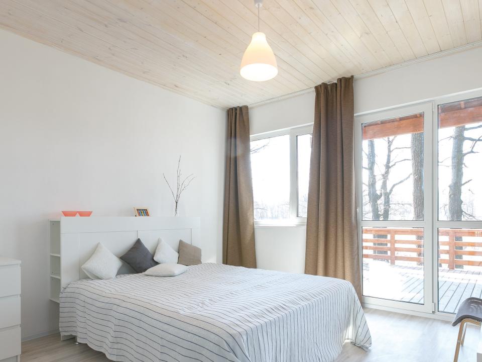 A bedroom with bed with white sheets, a white dresser and table, and green curtains under a ceiling with wooden paneling