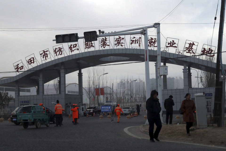 FILE - In this Dec. 5, 2018, file photo, residents pass by the entrance to the "Hotan City apparel employment training base" where Hetian Taida Apparel Co. has a factory in Hotan in western China's Xinjiang region. The Trump Administration is blocking shipments from Chinese company Hetian Taida Apparel, which makes baby pajamas sold at Costco warehouses, after the foreign manufacturer was accused of forcing ethnic minorities locked in an internment camp to sew clothes against their will. China's government has warned it will protect Chinese companies after Washington said enterprises may face legal trouble if they help carry out abuses in the Muslim northwestern region of Xinjiang. (AP Photo/Ng Han Guan, File)