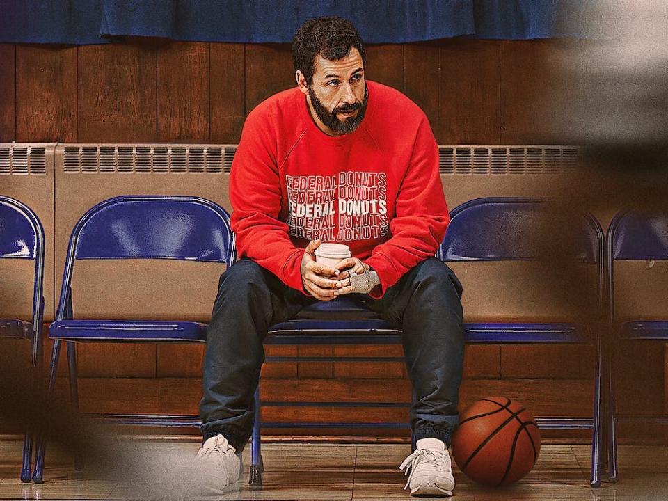 Adam Sandler sitting holding a coffee cup