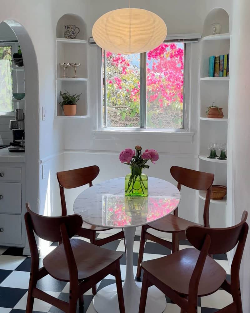 Paper mache oval lighting fixture, arched corner built in book cases, round white table with dark wood mid-century modern chairs, black and white checkered tile floor