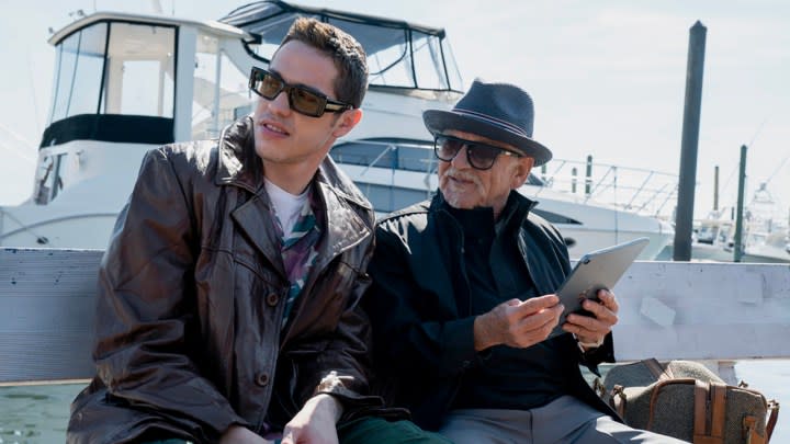 Pete Davidson and Joe Pesci sitting by the ferry in a scene from Bupkis on Peacock.