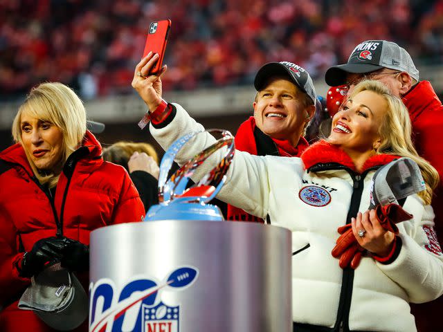 <p>David Eulitt/Getty</p> Tavia Hunt and Clark Hunt take a selfie with Andy Reid before being awarded the Lamar Hunt trophy after defeating the Tennessee Titans in the AFC Championship Game on January 19, 2020 in Kansas City, Missouri.