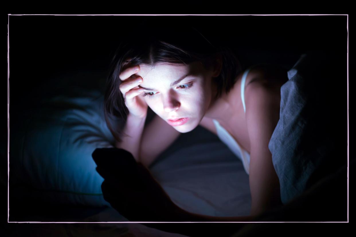  A teenage girl in a dark room lit up by her phone screen. 