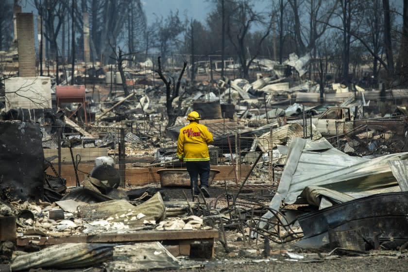 GREENVILLE, CA - AUGUST 08, 2021: Jaime Crane, an inspector with Cal Fire Shasta Trinity Unit, walks through the debris, searching for the material that the roofs of homes were made out of that burnt down in the town of Greenville as a result of the Dixie Fire. (Mel Melcon / Los Angeles Times)