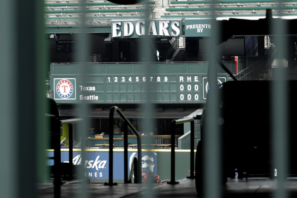 The manual scoreboard at T-Mobile Park in Seattle is seen through the bars of an entry gate, Thursday, March 26, 2020, on the day that would have been the Mariners' Opening Day baseball game against the visiting Texas Rangers. Earlier in the month, Major League Baseball called off the start of the season due to the outbreak of the new coronavirus. (AP Photo/Ted S. Warren)