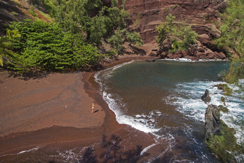 FILE - In this Sept. 24, 2014, file photo, a woman walks on the red sand beach at Kaihalulu Bay in Hana, Hawaii. So many tourists are flocking to Maui now that coronavirus pandemic concerns have eased in the United States that islanders are feeling overwhelmed and Maui's mayor is begging airlines to cut back on the number of people they fly to the island. (AP Photo/Marco Garcia, File)