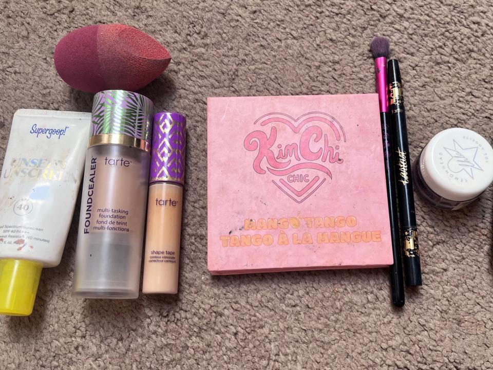 Supergoop sunscreen, Tarte foundation and concealer, a beauty sponge, a Kim Chi palette, two eye-shadow brushes, eye glitter, Urban Decay All-Nighter spray, and a pink lipstick