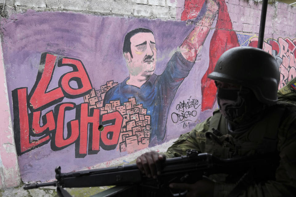 Soldiers patrol past a political movement's mural that reads in Spanish, "The fight" in a residential area on the south side of Quito, Ecuador, Friday, Jan. 12, 2024. In the wake of the apparent escape of a powerful gang leader from prison, President Daniel Noboa decreed on Monday a national state of emergency, a measure that lets authorities suspend people’s rights and mobilize the military. (AP Photo/Dolores Ochoa)