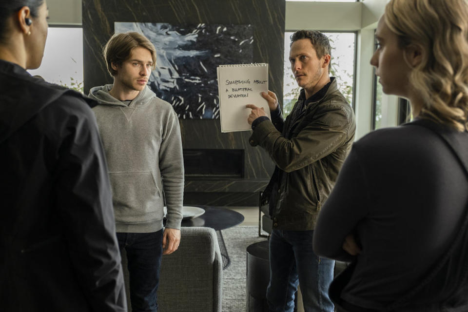 Bryan holds a sign next to a young man as Finola and a woman look at him