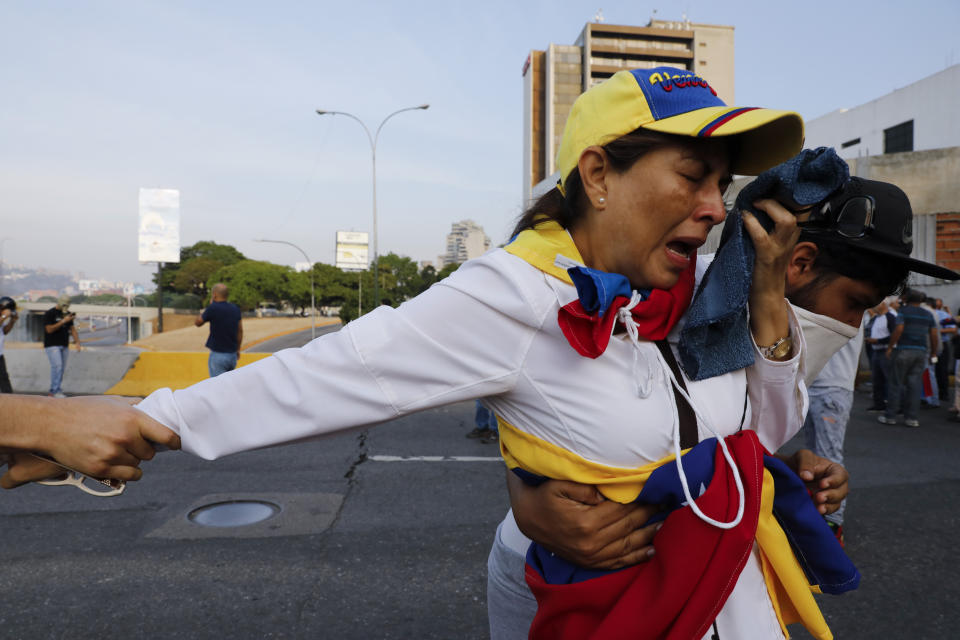 Una mujer asfixiada por gas lacrimógeno es ayudada por compañeros opositores al presidente Nicolás Maduro afuera de la base aérea de La Carlota en Caracas, Venezuela, el martes 30 de abril de 2019. (AP Foto / Ariana Cubillos)