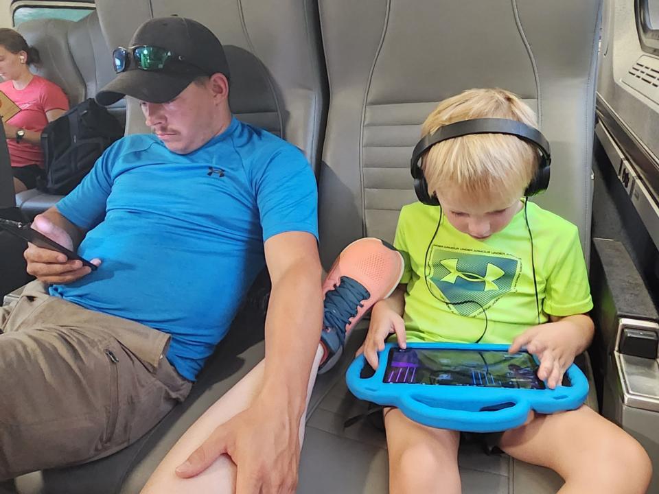 Man and child sitting on Amtrak train seats comfortably, both holding electronic devices