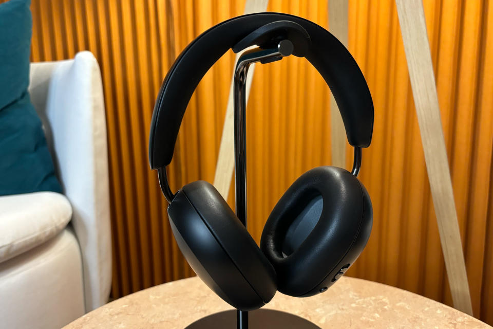 <p>Black headphones sitting on a stand on a small table.</p>
