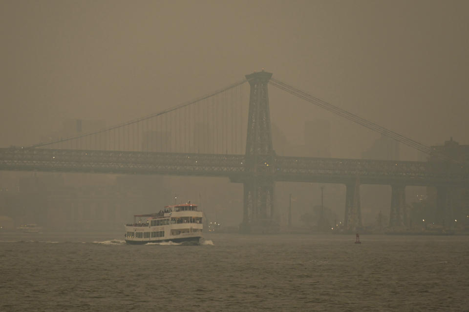 A Circle Line ferry sails past the Williamsburg Bridge as the Manhattan skyline is shrouded in smoke.