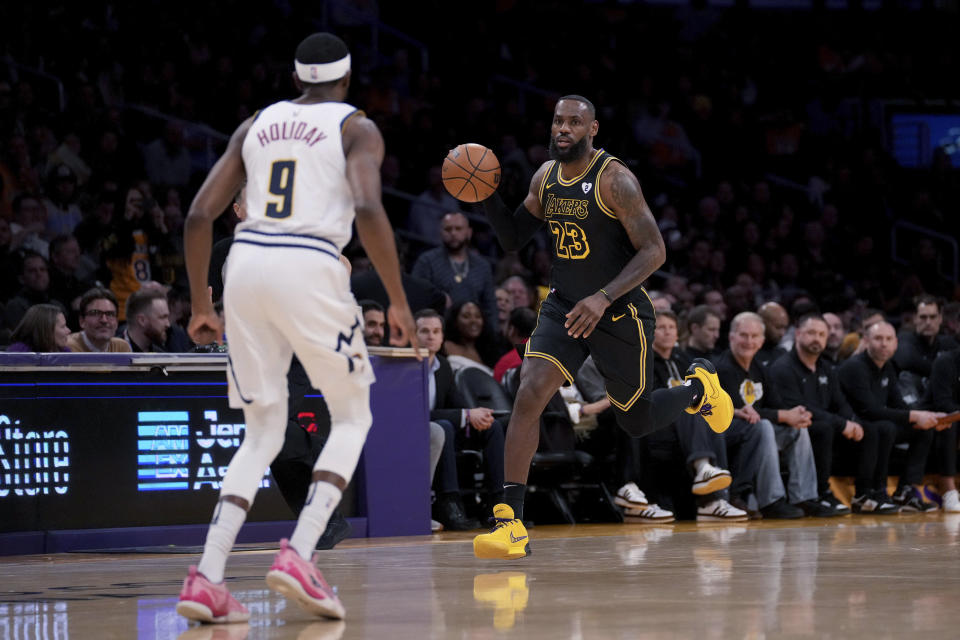 Los Angeles Lakers forward LeBron James brings the ball up as Denver Nuggets forward Justin Holiday (9) watches during the first half of an NBA basketball game in Los Angeles, Thursday, Feb. 8, 2024. (AP Photo/Eric Thayer)