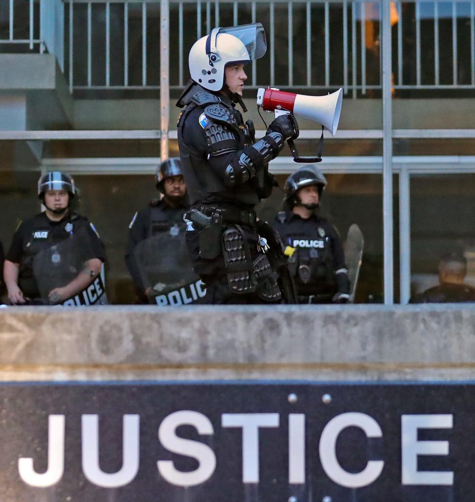 An Akron police officer in riot gear announces the 9 p.m. curfew outside the Harold K. Stubbs Justice Center on Monday.