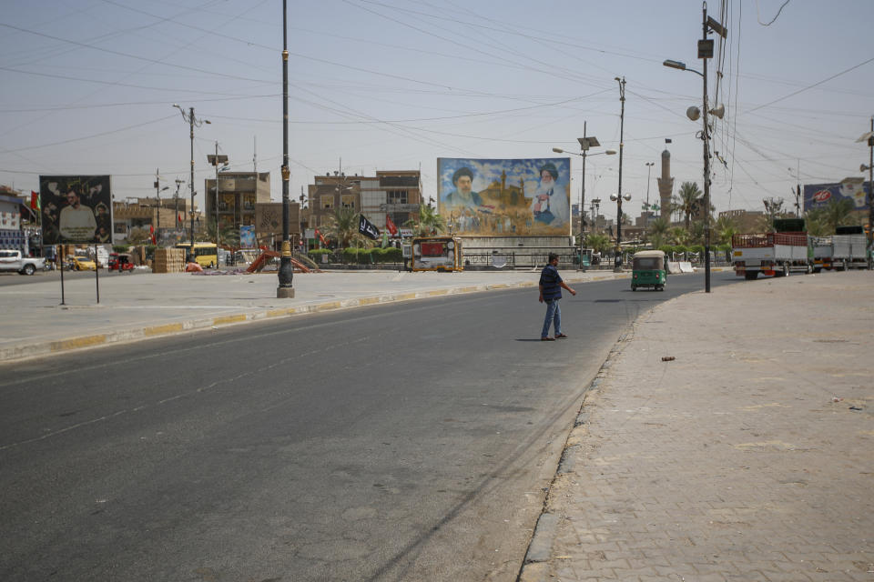 People navigate a street with a poster of Shiite religious leaders Mohammed Sadiq al-Sadr, right, and his relative, Mohammed Baqir al-Sadr, left, is displayed in Baghdad's Shiite enclave of Sadr City, in Baghdad, Iraq, Thursday, Aug. 4, 2022. (AP Photo/Anmar Khalil)