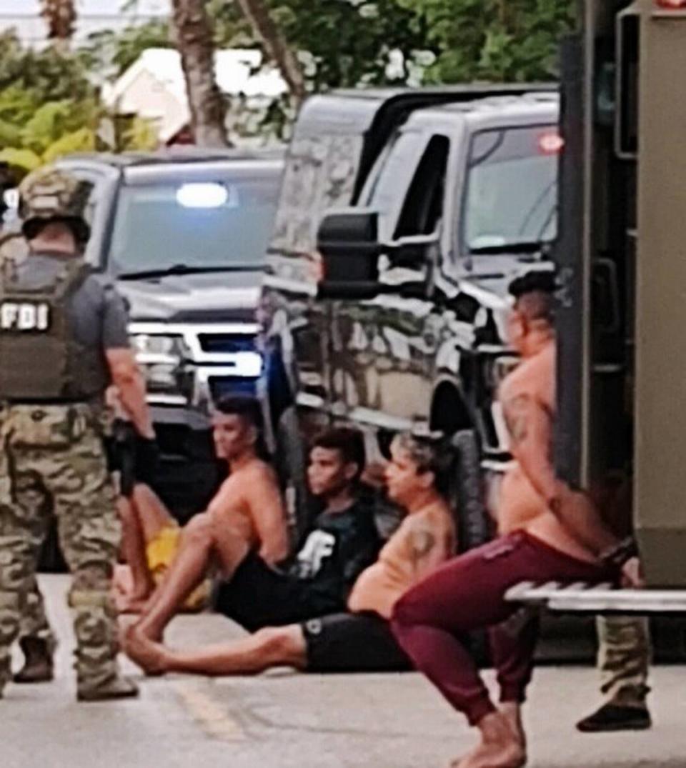 Several men sit handcuffed on a Geiger Key street following an FBI raid Friday, Dec. 16, 2022.