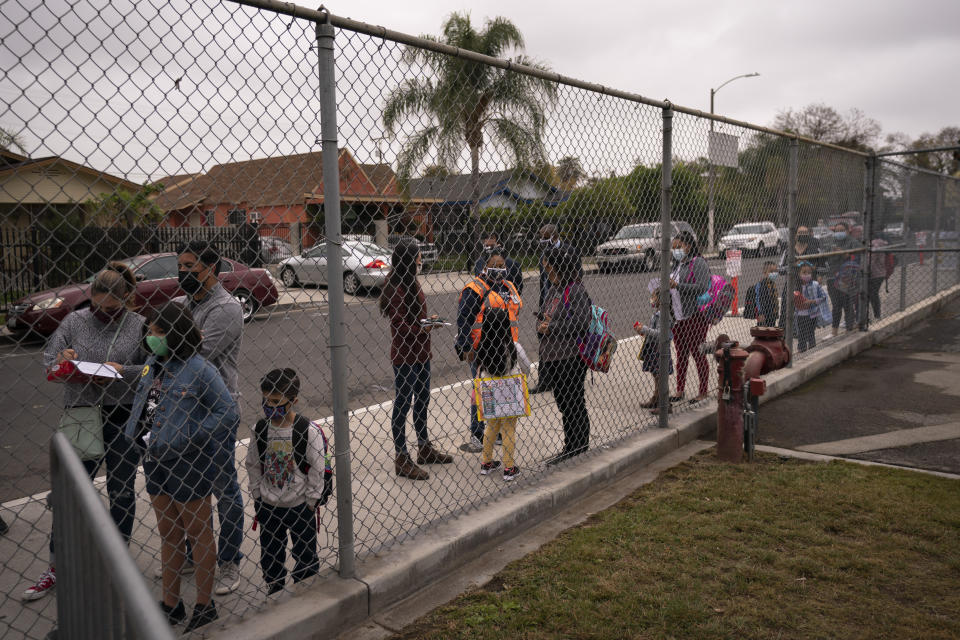 Parents and students wait in line to check in on the first day of in-person learning at Heliotrope Avenue Elementary School in Maywood, Calif., Tuesday, April 13, 2021. More than a year after the pandemic forced all of California's schools to close classroom doors, some of the state's largest school districts are slowly beginning to reopen this week for in-person instruction. (AP Photo/Jae C. Hong)