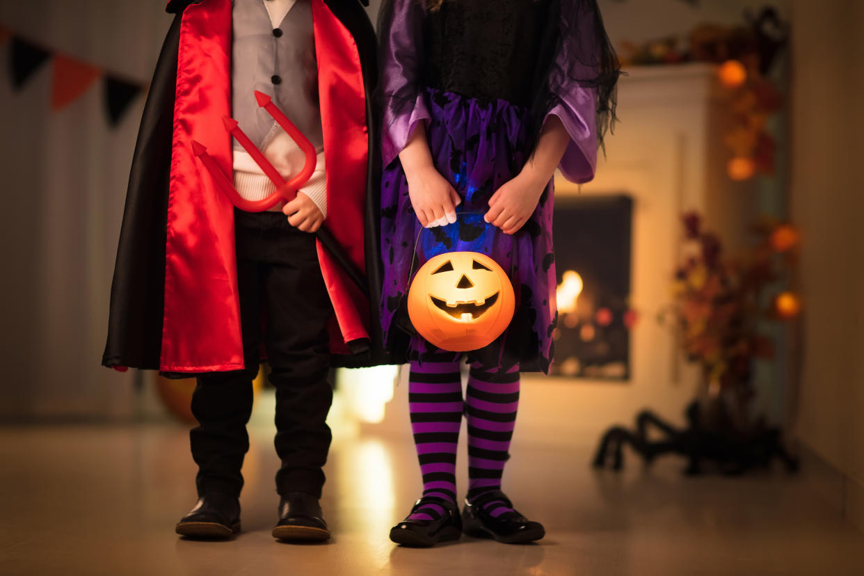 Little girl in witch costume and boy dressed up as vampire on Halloween trick or treat. Children trick or treating with candy bucket. Kids celebrate Halloween at fireplace with pumpkin and lantern.