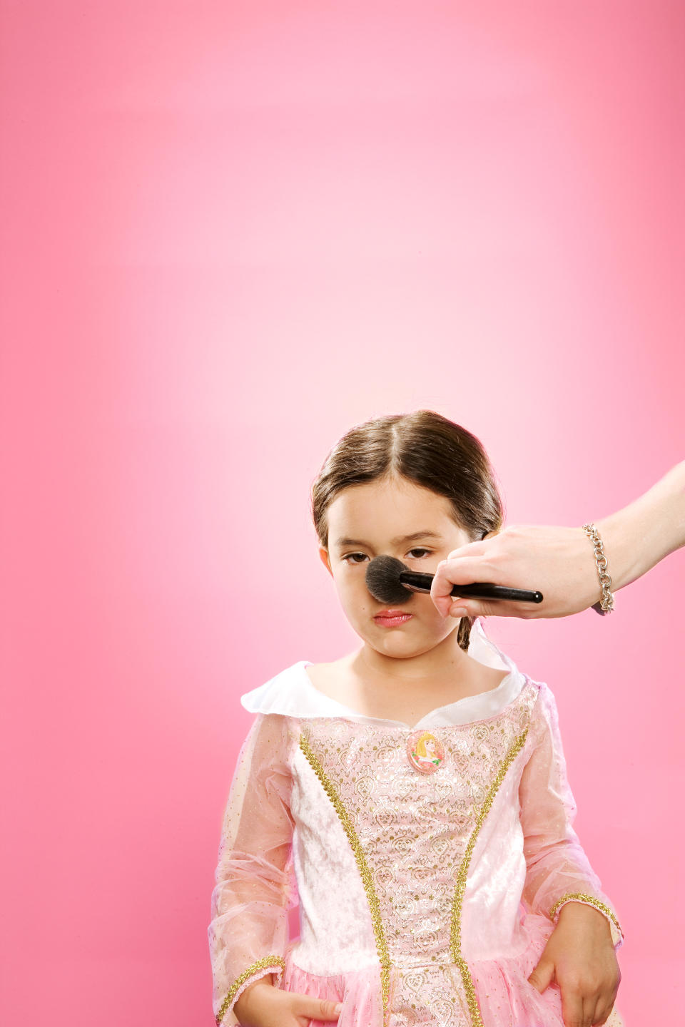 Someone putting makeup on a little girl who's dressed as a princess